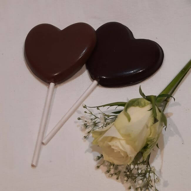 2 heart shaped lollies next to wedding button hole flower. Heart Shaped Chocolate Lolly. 